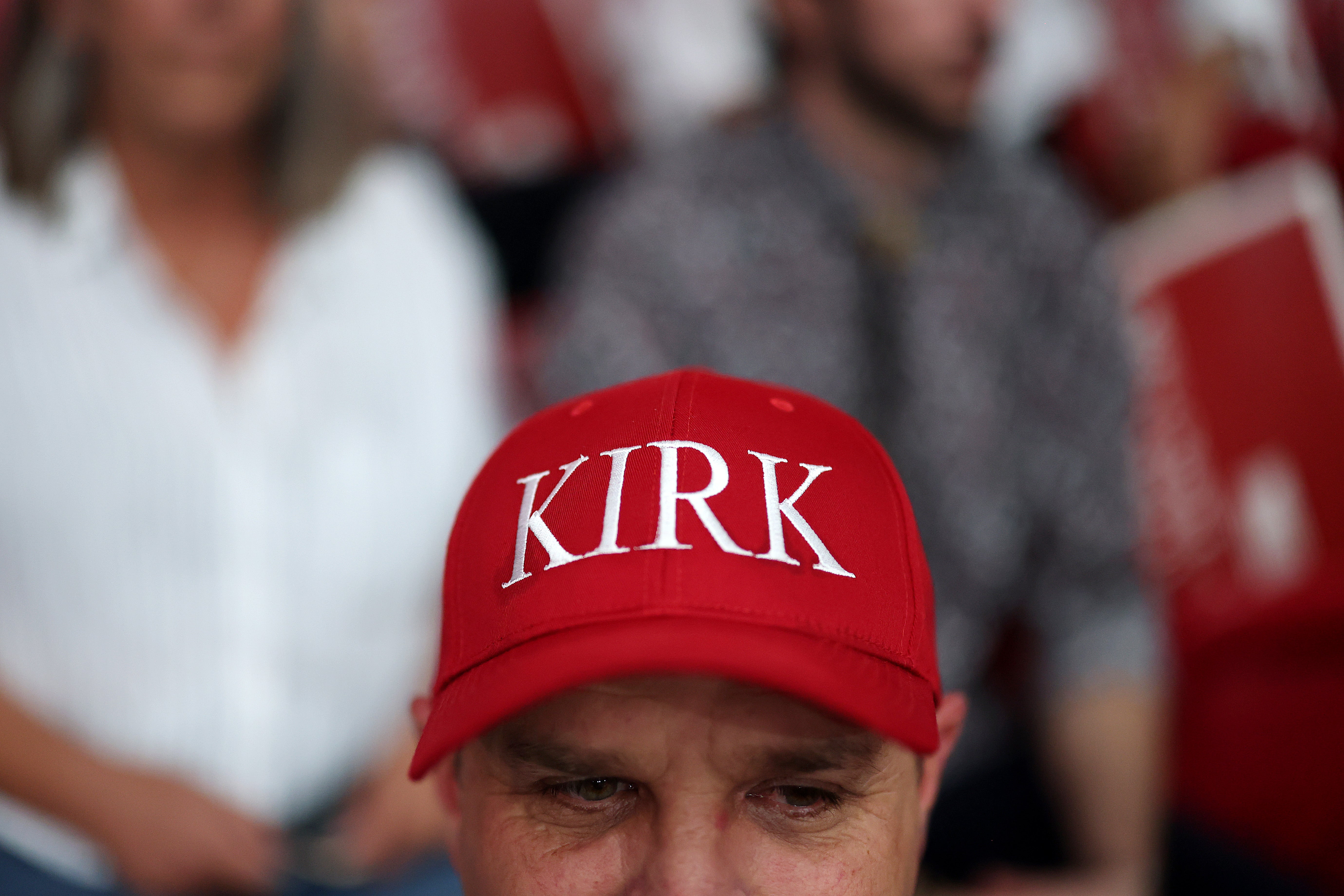 An attendee wearing a red 'Kirk' hat sits in the stands ahead of the memorial service