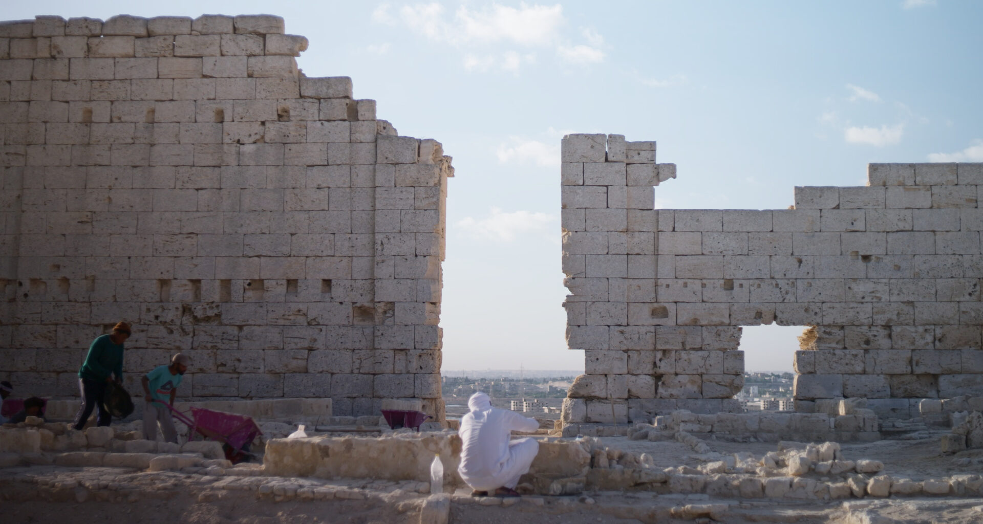 Archaeologists excavate a site with a tall wall in Egypt.