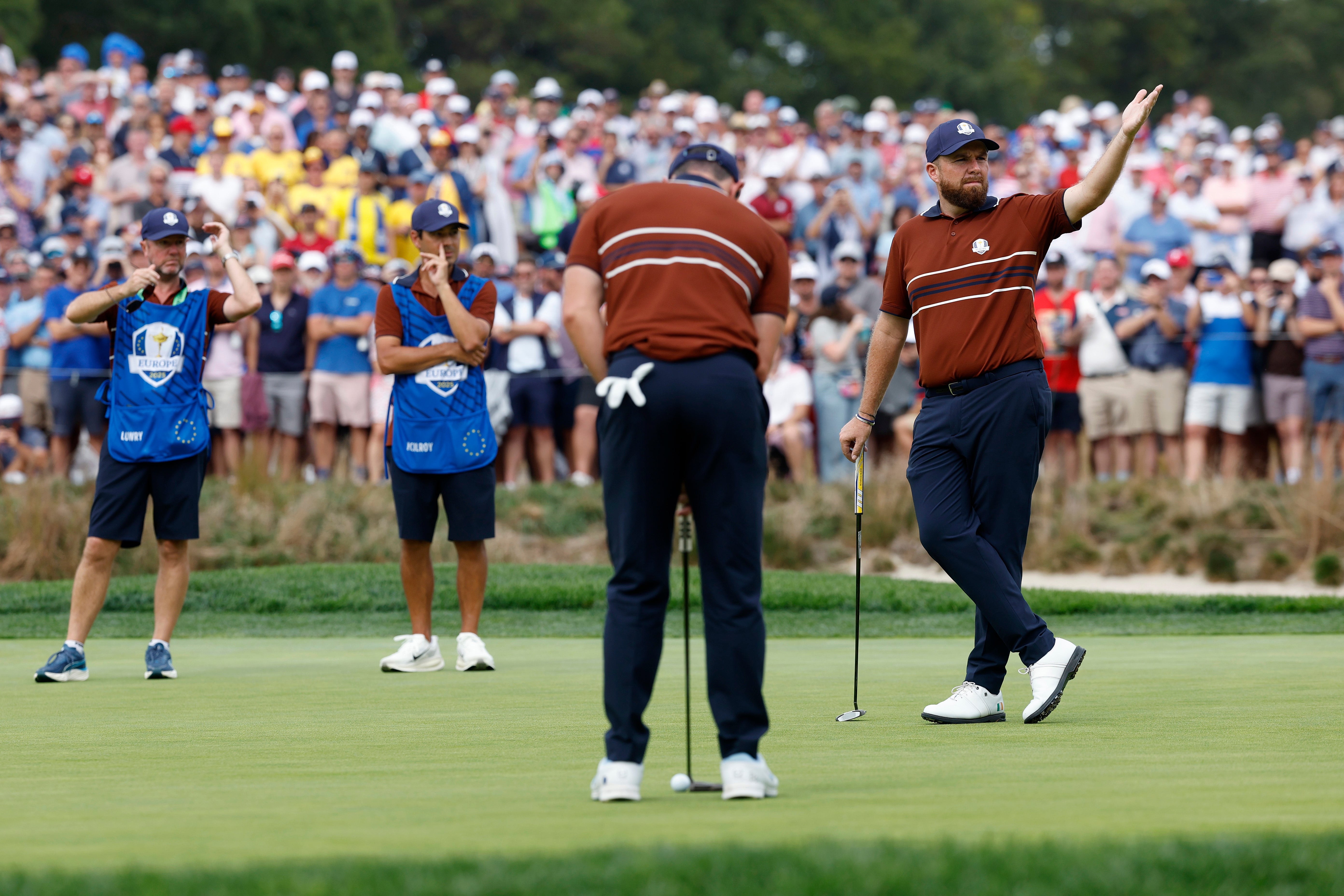Shane Lowry gestures at noisy fans while Rory McIlroy lines up a putt