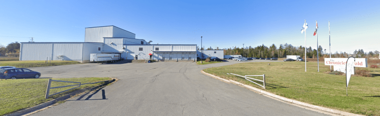 A low white building is to the left. To the right is a sign reading "The Chronicle-Herald, with three flag poles next to it.