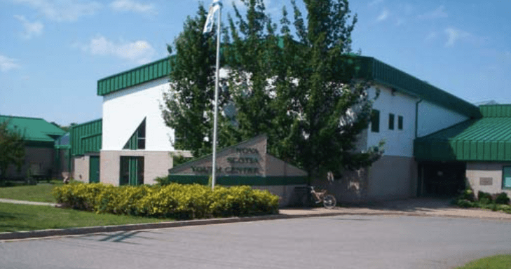 A photo of the Nova Scotia Youth Centre in Waterville. The building is white with green trim. A few trees are planted out front.