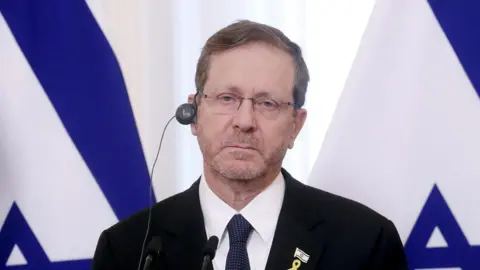 EPA/Shutterstock Isaac Herzog, in a dark suit, white shirt and blue tie, stares impassively at the camera. He has an earpiece in his ear.