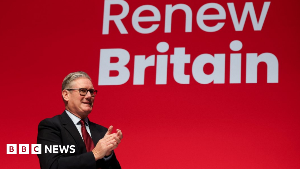 Sir Keir Starmer stands in front of a giant red screen with the slogan Renew Britain. He is wearing a dark suit with a white shirt and a red tie. He is applauding Chancellor Rachel Reeves, not shown.