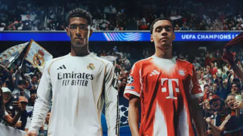 Electronic Arts Video game versions of Jude Bellingham and Jamal Musiala standing next to each other looking towards the camera. The game version of Bellingham is wearing his Real Madrid kit and Musiala in his Bayern kit.