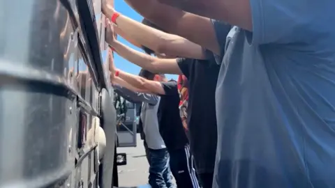 EPA/Shutterstock A still frame showing people with their hands up leaning against a bus from a video made available by the US Immigration and Customs Enforcement via the Defense Visual Information Distribution Service (DVIDS) shows an immigration raid at the Hyundai-LG vehicle assembly plant in Ellabell, Georgia, USA, 04 September 2025
