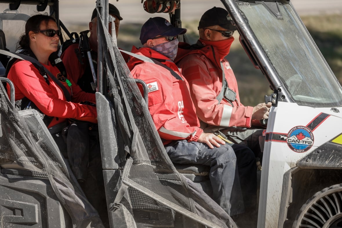 Three people in red jackets, ballcaps and sunglasses ride in an ATV.