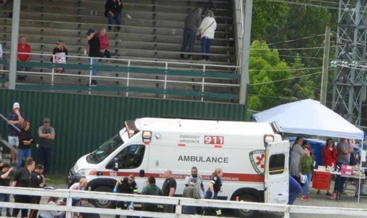 distance shot of ambulance pulled up between grandstand and perimeter fence. People standing all around