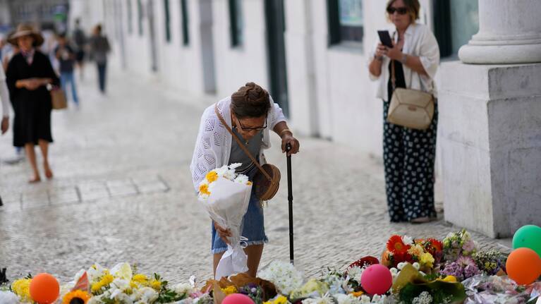 An elderly woman places a bouquet of flowers at a tribute to those that perished in the Gloria funicular, a tourist streetcar that derailed and crashed, in Lisbon, Saturday, Sept. 6, 2025.