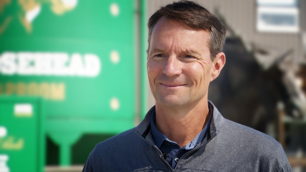 A smiling man in front of a green background.
