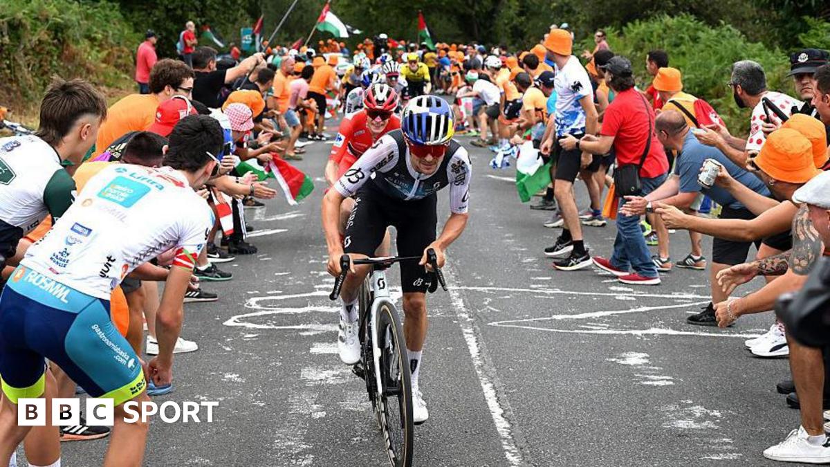 Tom Pidcock riding in the Vuelta a Espana as spectators stand on the road and encourage cyclists