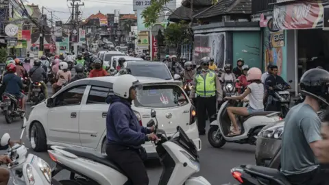 Getty Images A road in Bali lined by shops, crowded with people on motorcycles and cars