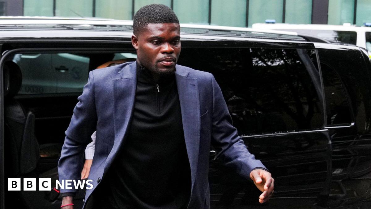 Thomas Partey wears a navy blue blazer and black shirt. He walks from a black car towards the camera.