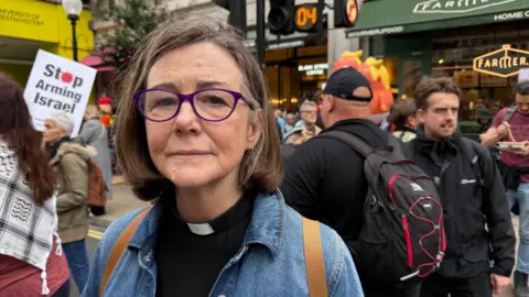 She is wearing glasses and a light blue denim jacket. She has straight, dark brown hair cut into a bob.