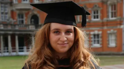 Simon Hanning Molly at her graduation, wearing a cap and gown. She is smiling at the camera and has long, red hair.