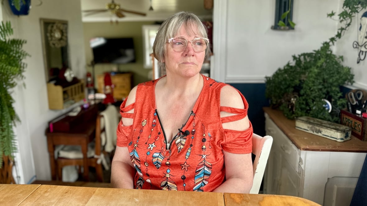 A omwan in an orange shirt sits at a kitchen table and stares out of the window.