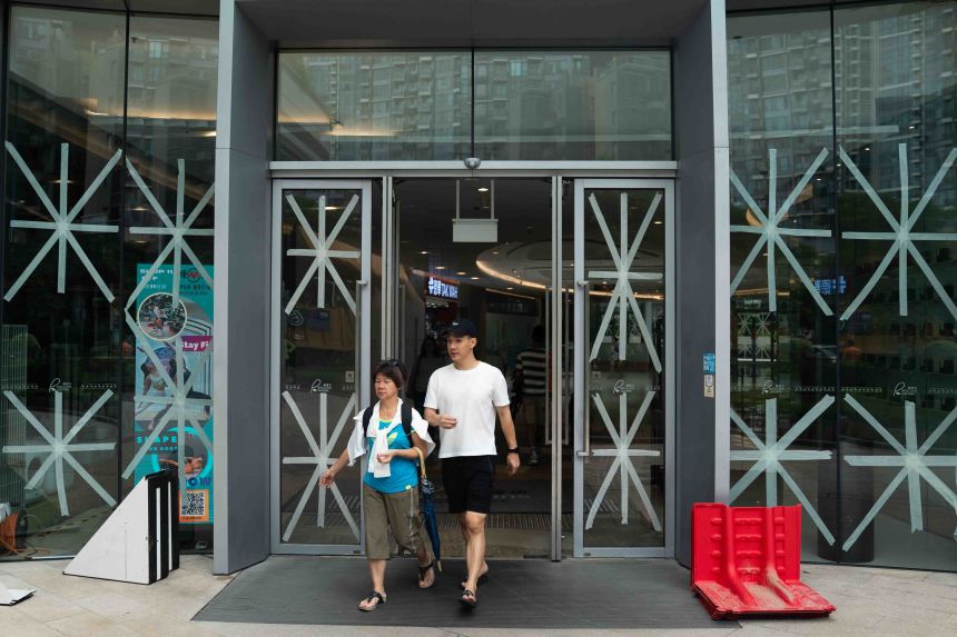 People walk past a shopping mall with their windows taped with X signs as a precautionary measure in Hong Kong on September 23, 2025.