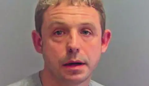 Norfolk Police Mug shot of Shaun Gilder looking directly at the camera. He has bleached blonde hair and is wearing what appears to be a prison issue sweat shirt.