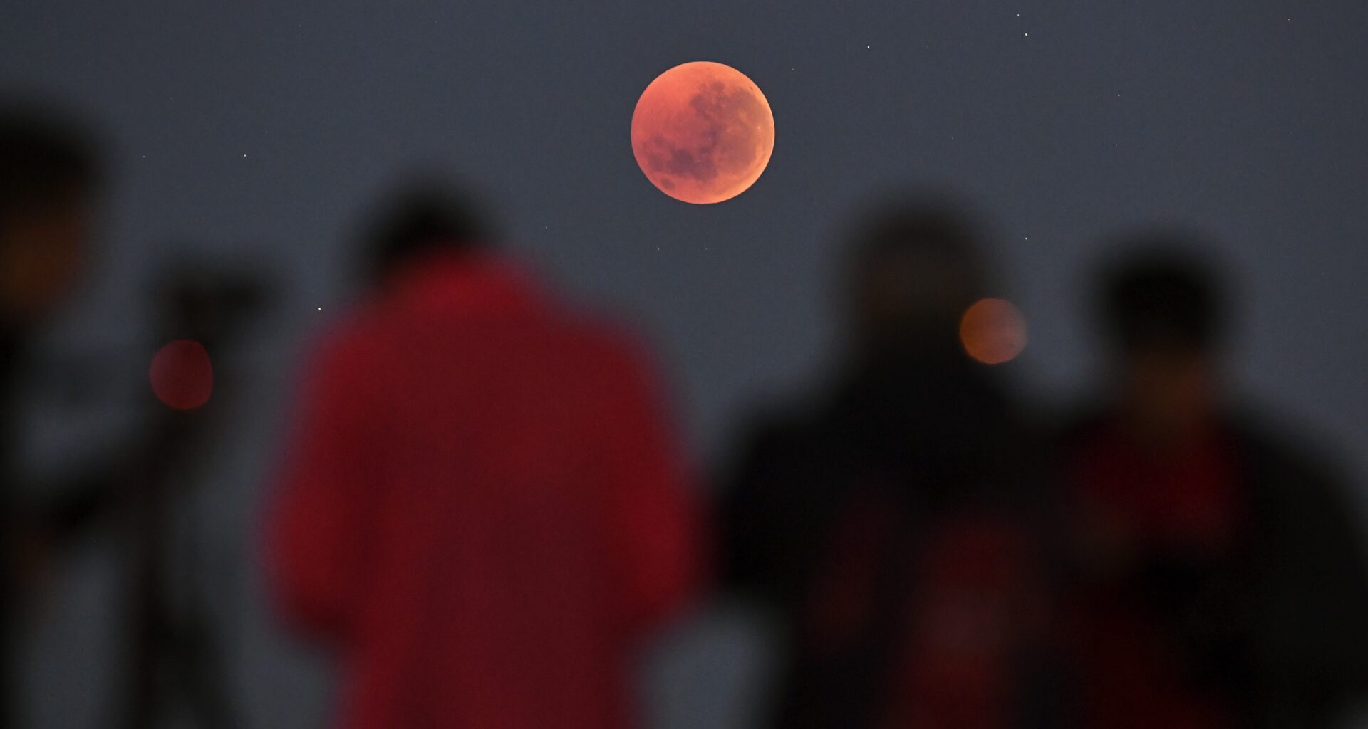 people stand and look at a total lunar eclipse blood moon high in the sky.