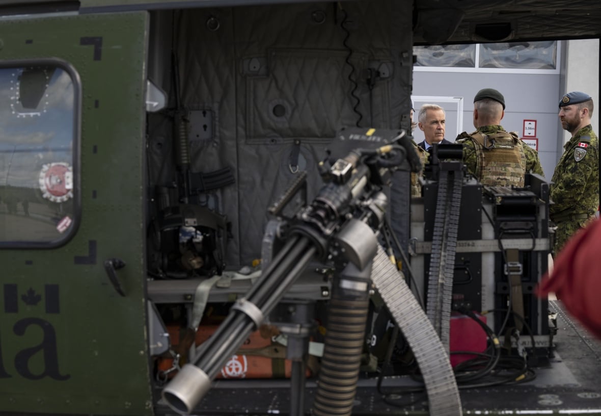 An armoured vehicle can be seen in the foreground, with a machine gun hanging out of it. Men stand behind it and seem to be in conversation.