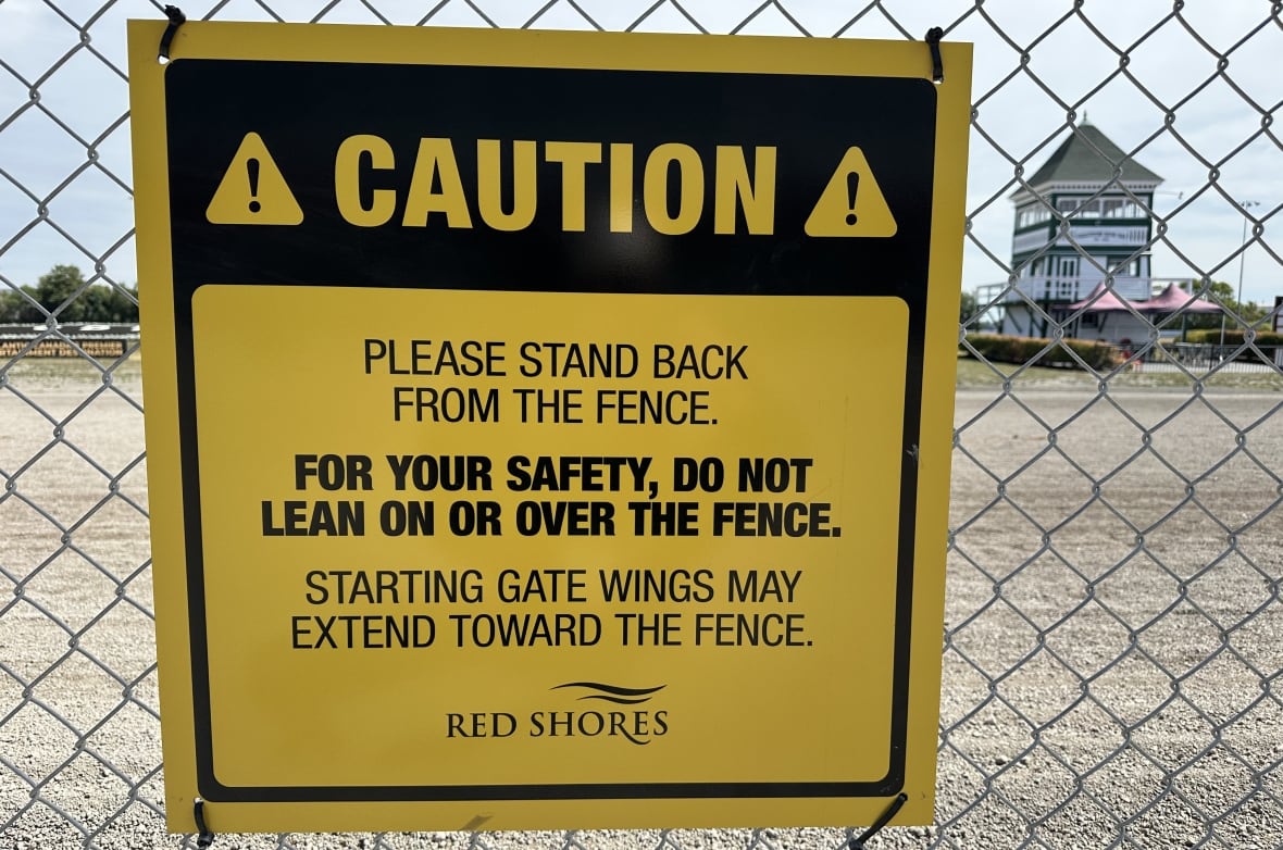yellow sign affixed to perimeter fence at Charlottetown raceway cautions people to stand back from the fence