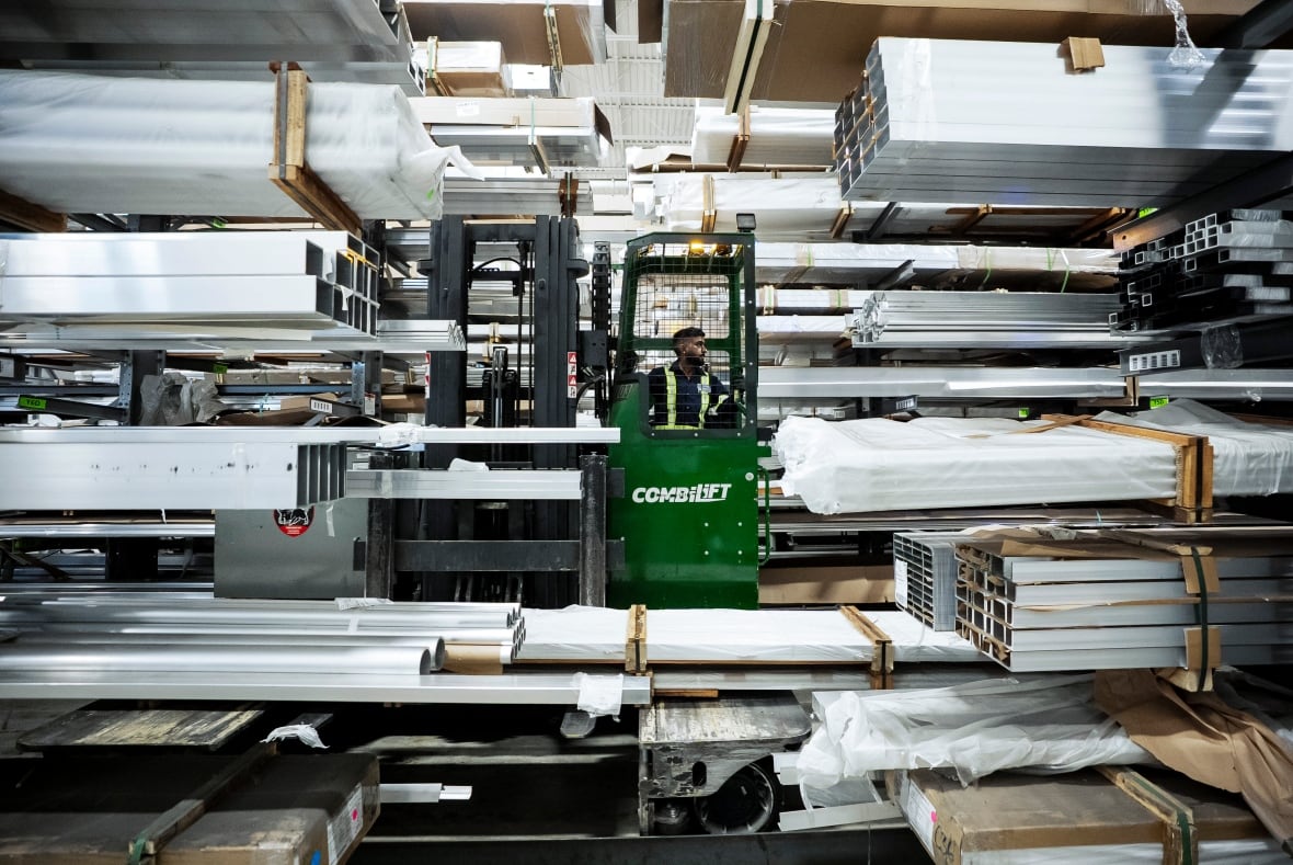 A worker in a machine is seen working on a floor among a lot of shiny blocks of aluminum