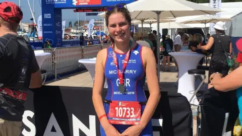 Family handout Lily at a triathlon event before she got ill. She has a blue outfit on and a medal around her neck. 