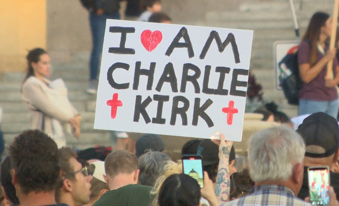 A sign is held up in a crowd of people. The words on it say "I am Charlie Kirk."