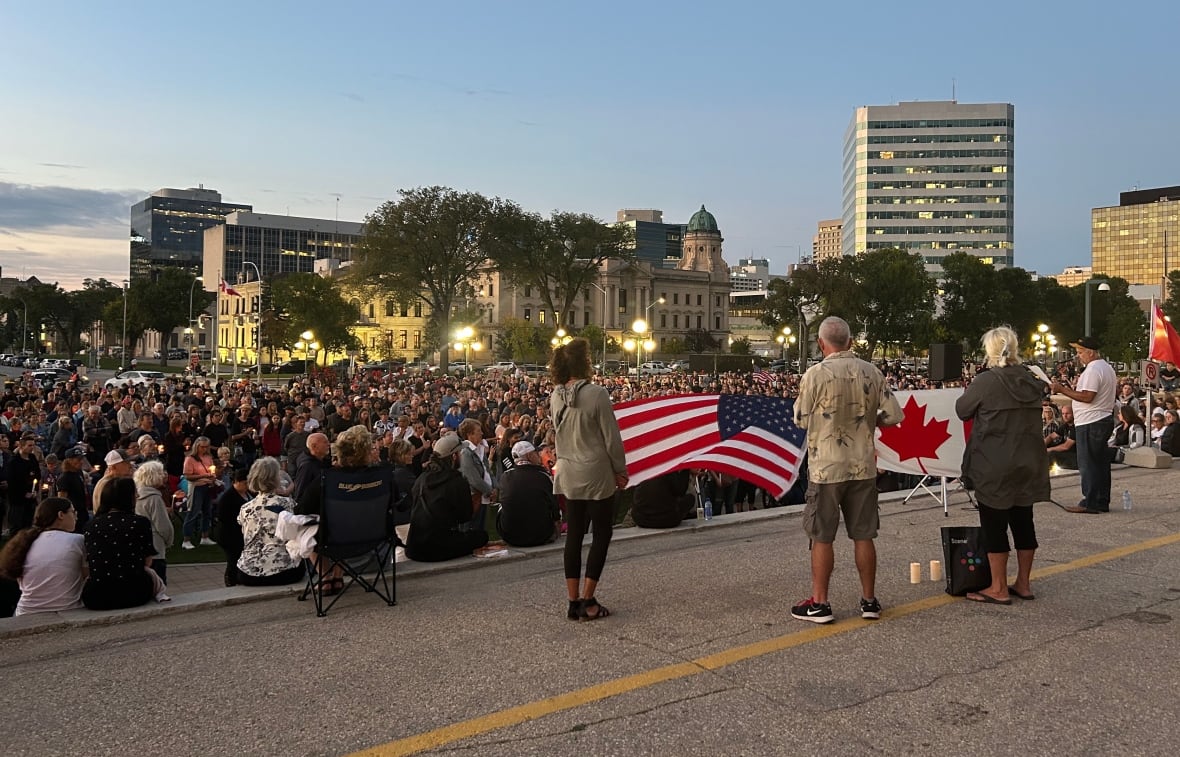 A crowd of people are seen in the evening light, holding candles.