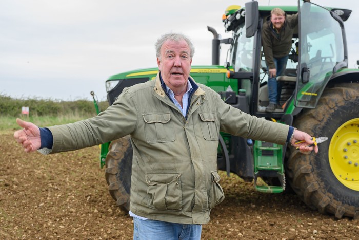 Jeremy Clarkson stood in front of a large green tractor with his hands spread outwards.