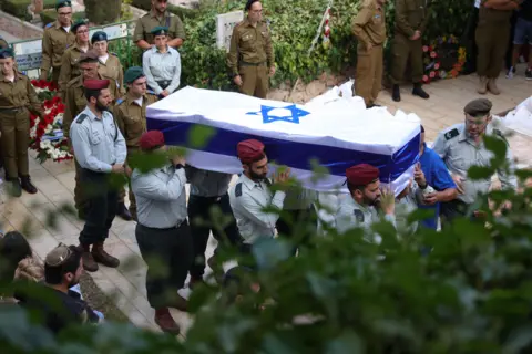 EPA Israeli soldiers carry the coffin of Israeli soldier Tal Cohen during his funeral at Mount Hertzel military cemetery in Jerusalem. The Israeli flag covers the coffin. The photo is taken slightly from above, looking down on the occasion.