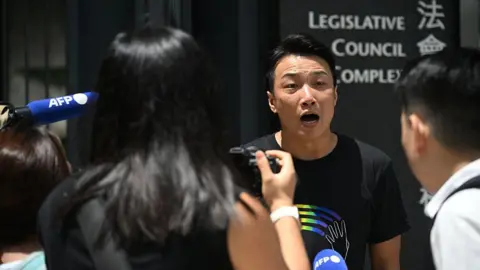 Getty Images Jimmy Sham wearing a black shirt with a rainbow logo speaks to reporters outside of the Legislative Council Complex in Hong Kong