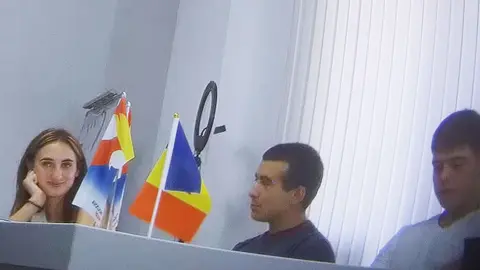 BBC A woman with long brown hair (Alina Juk) smiles at the group surrounding her - they are sat around a large table and two flags are in view, one of which is the Moldovan flag in colours of red, yellow and blue 