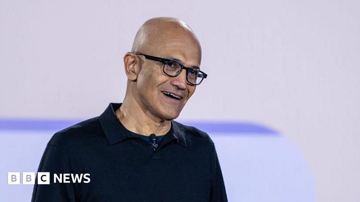 Satya Nadella smiling, wearing glasses and a black sweater