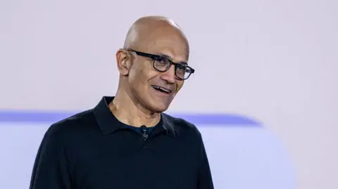 Getty Images Satya Nadella smiling, wearing glasses and a black sweater