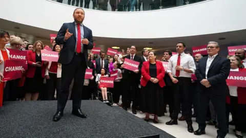 PA Media Ian Murray stands on stage in a suit and red tie and men and women in suits and smart clothes hold red signs saying change
