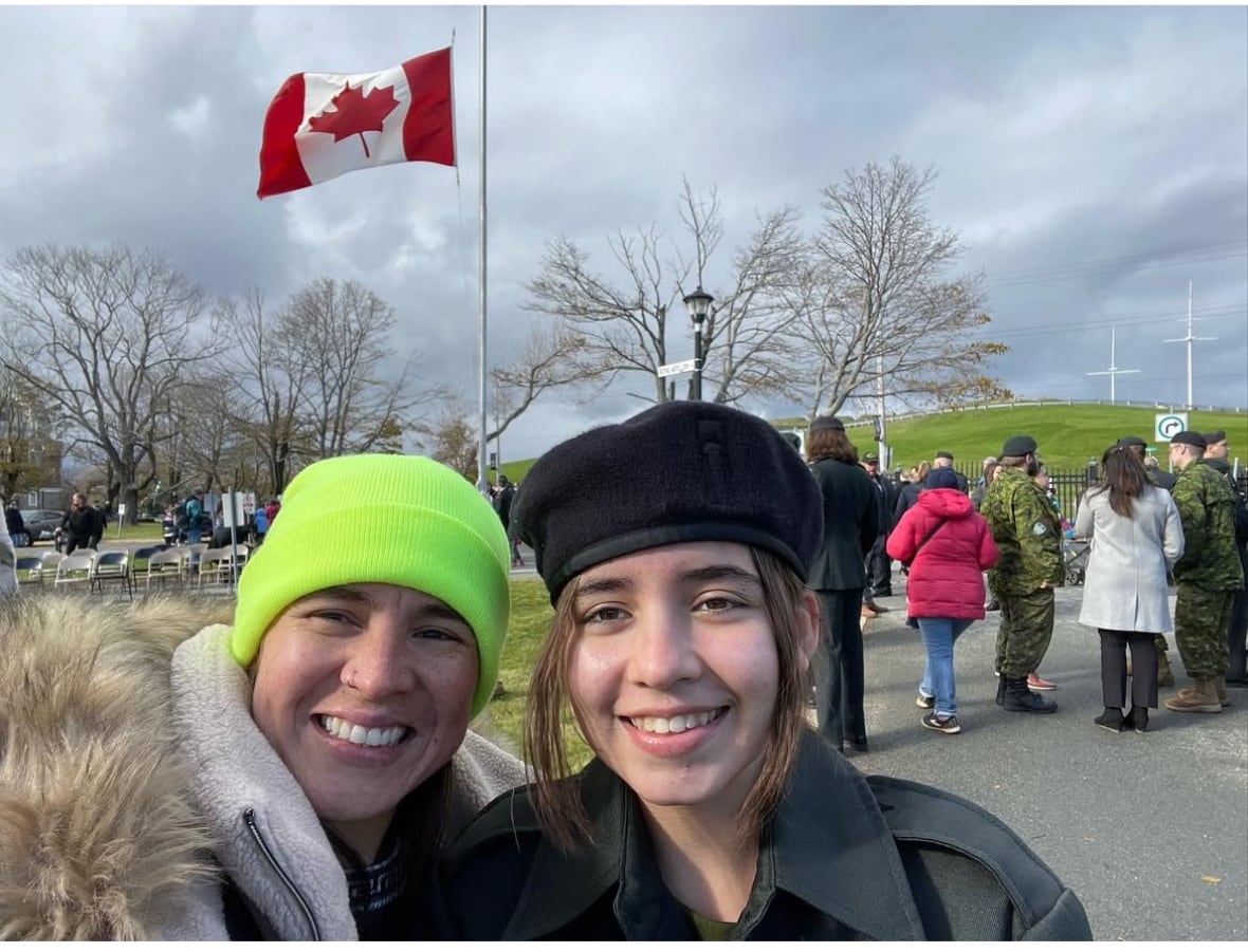 Two women stand near a Canadian flag. 