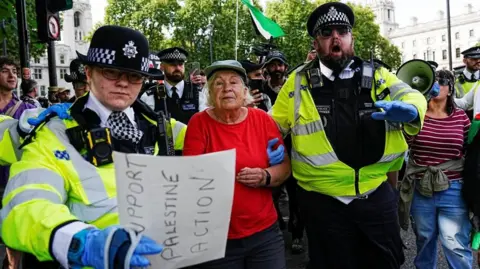 Reuters Two police officers escort a woman in a red shirt through a crowd