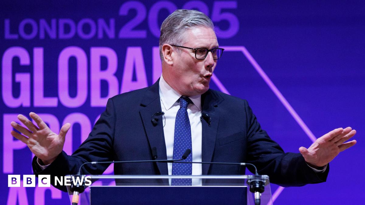 A man with grey hair and glasses speaks at a glass podium, gesturing with two open hands. Behind him reads "London 2025: Global Progress Action Summit", emblazoned on a purple background.