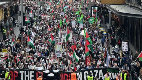 Getty Images A dense crowd of people fill a street, many of them waving placards and Palestinian flags