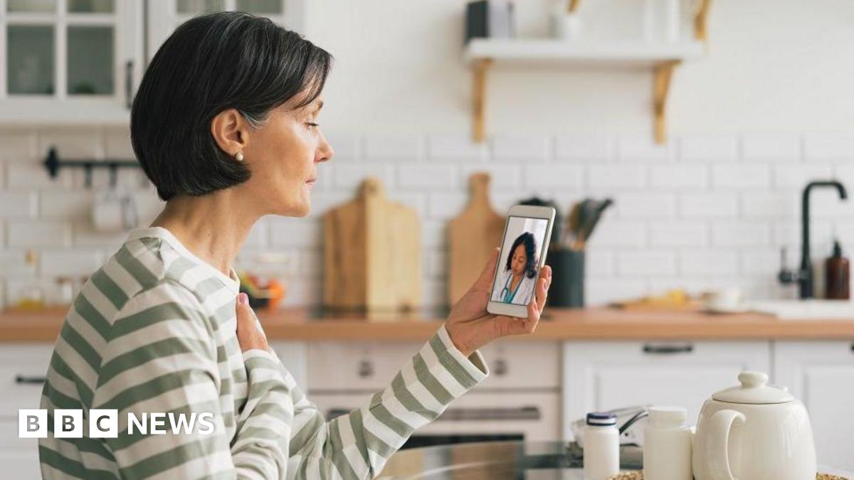 A woman wearing a striped top sits in her kitchen while on a video call with a doctor.