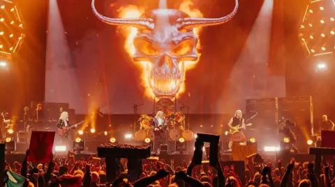 Bleecker Street/Sony Pictures Spinal Tap playing live while fans holding up minituare Stone Henge replicas