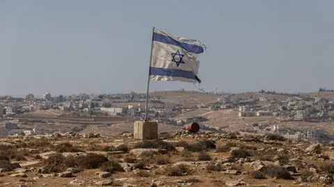 Getty Images An Israeli flag is planted into the ground, in a barren, hilly landscape in the occupied West Bank