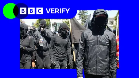 Getty Images A group of people dressed in all-black, with their eyes and mouths covered by sunglasses and masks, march forward during an anti-fascist protest