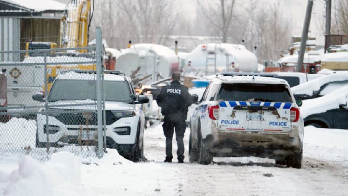 A police officer stands between two parked police vehicles in a snowy lot.