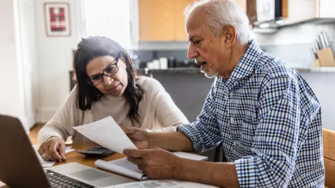 Getty Images A man and a woman review paperwork at a kitchen table.