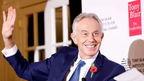 Getty Images Former UK Prime Minister Tony Blair smiles and waves against a backdrop sign saying 'Tony Blair on leadership'.