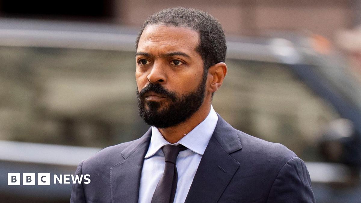 Noel Clarke, arriving at the High Court on Tuesday, wearing a grey suit and white shirt. He has short black hair and a close cropped beard and moustache.