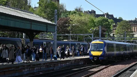 Getty Images A ScotRail train arrives at Waverly station in Edinburgh in the sunshine, the castle in the background. People are making their way off the train and up the platform.