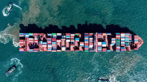 Getty Images An aerial view of a cargo ship at sea, with hundreds of containers visible on its desk