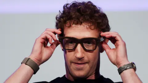 Reuters Meta boss Mark Zuckerberg holds a pair of black-framed AI-powered glasses to his face at the company’s annual Meta Connect conference.